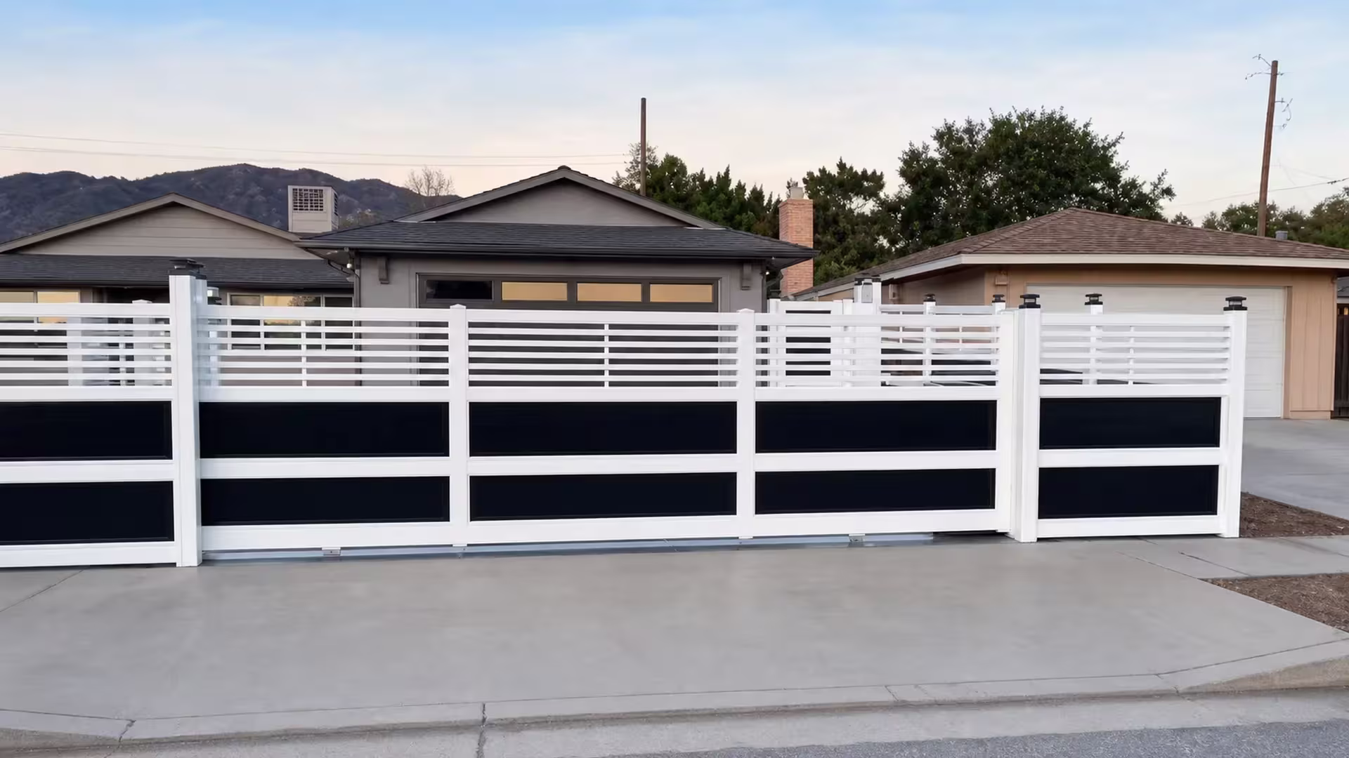 A street curb leads to this White vinyl privacy fence with acrylic set before a garage and distant mountains