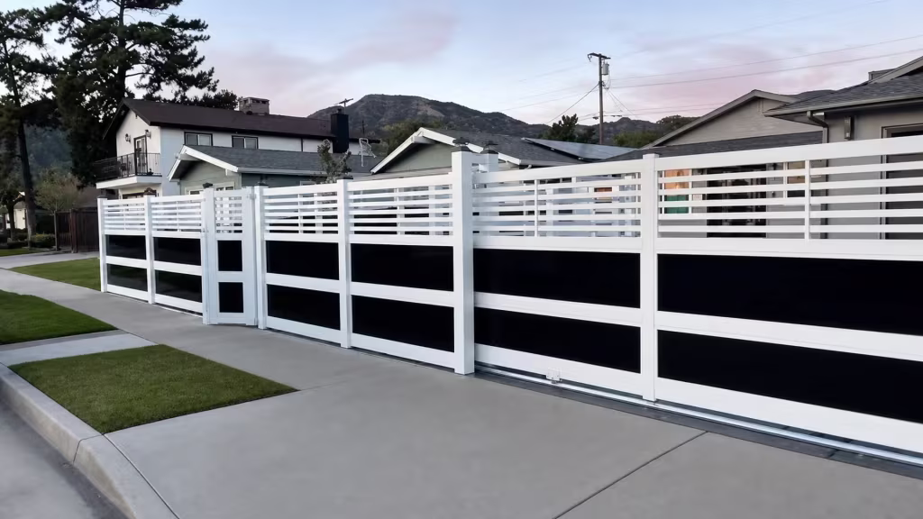 A narrow pedestrian gate opens this White vinyl privacy fence with acrylic beside a strip of front lawn