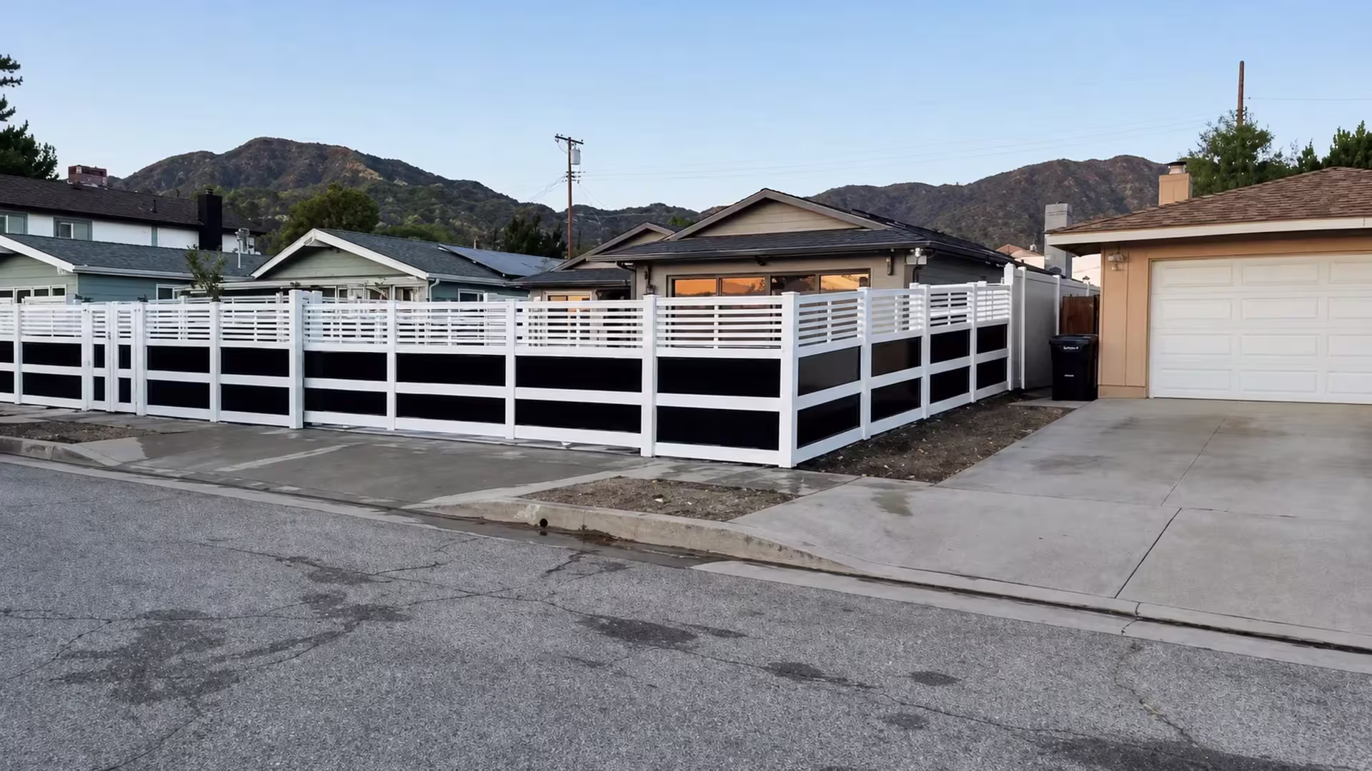 White vinyl privacy fence with acrylic turns the front yard corner beneath a distant mountain skyline