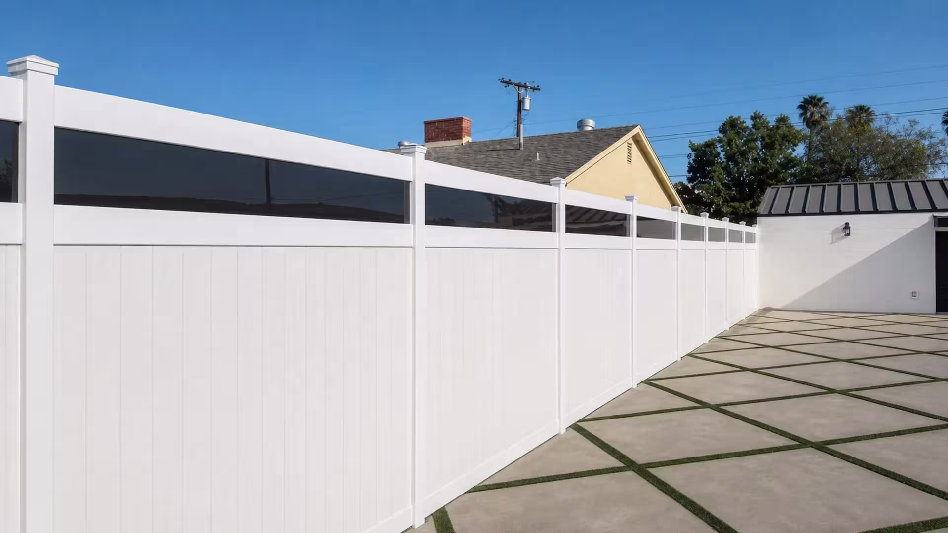 A utility pole and palms rise above this White vinyl privacy fence with acrylic lining a paved courtyard