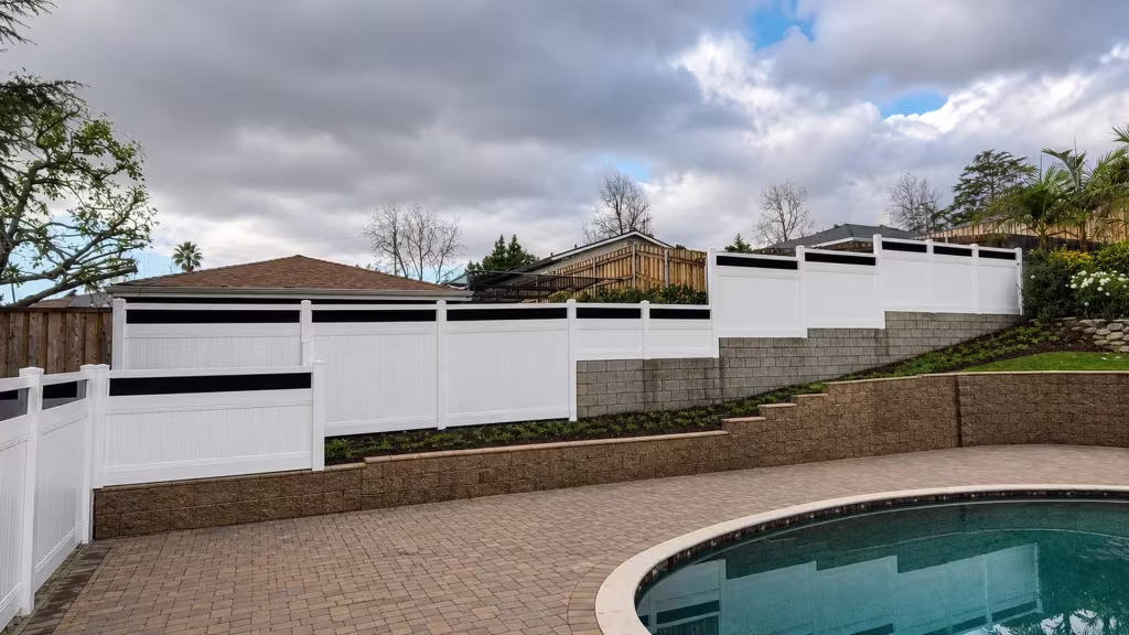 Terraced pool ground steps down beside this White vinyl privacy fence with acrylic falling toward a block wall
