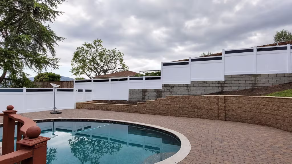 Stacked stone and concrete block retaining walls carry this White vinyl privacy fence with acrylic climbing in tiers