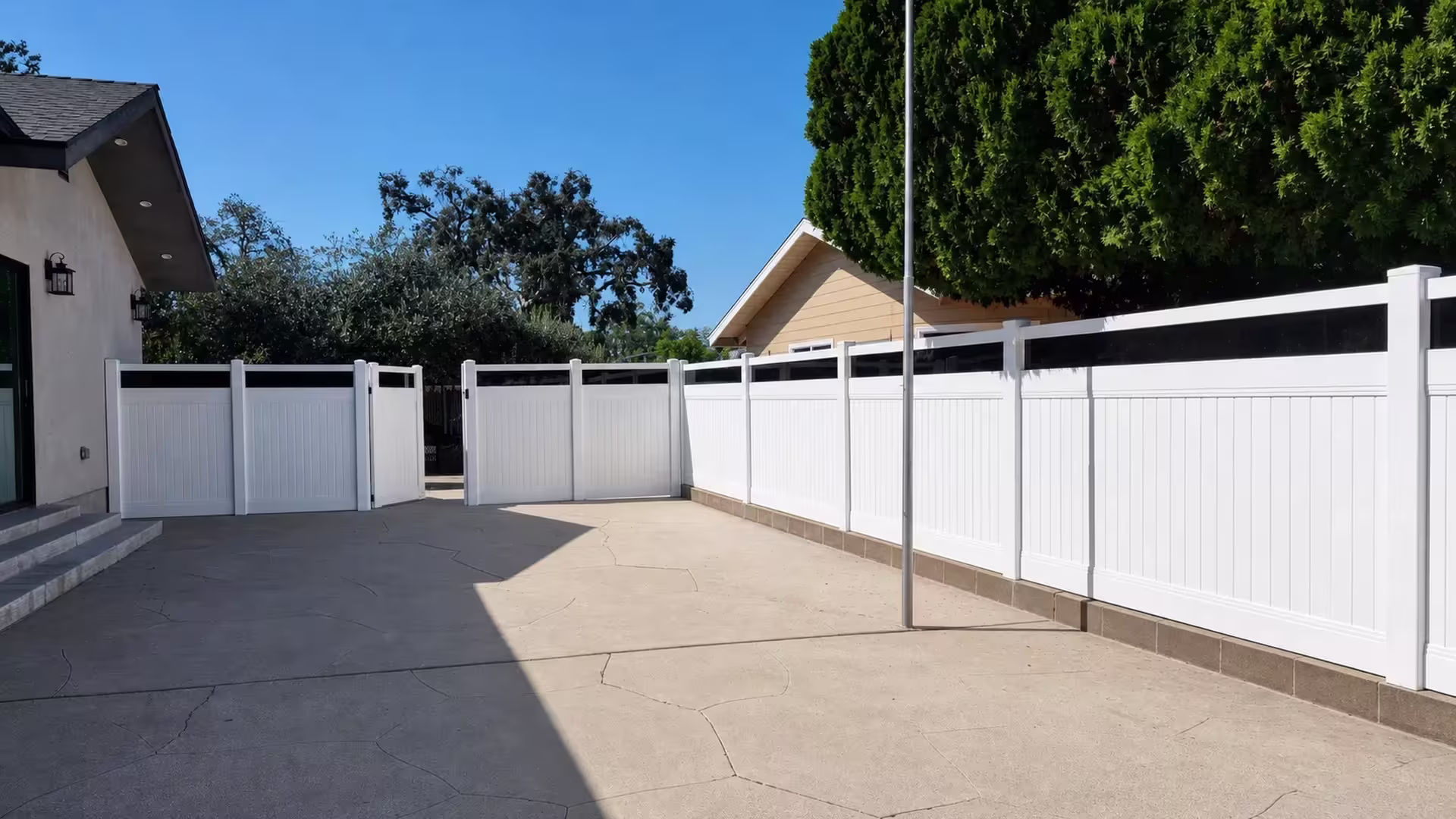Central metal pole stands before this White vinyl privacy fence with a dark smoke acrylic top band