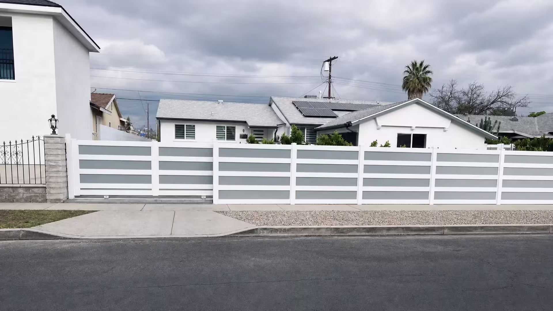 Solar panels top the roofline above this White vinyl privacy fence with pale blue gray acrylic panels