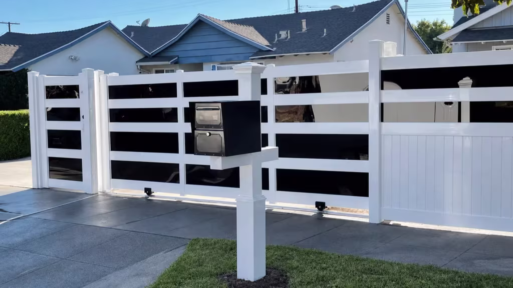 Freestanding mailbox stands beside this White vinyl privacy fence and gate with stacked dark acrylic bands
