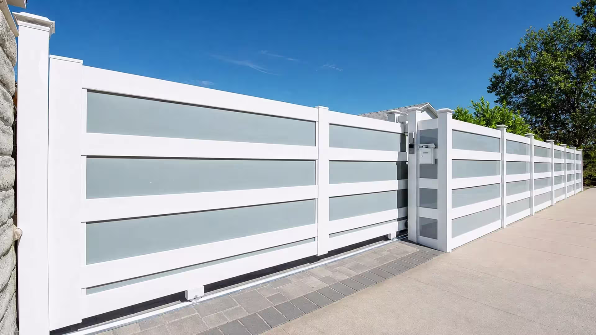 Stone wall edge meets this White vinyl privacy fence with frosted acrylic and a tracked sliding gate