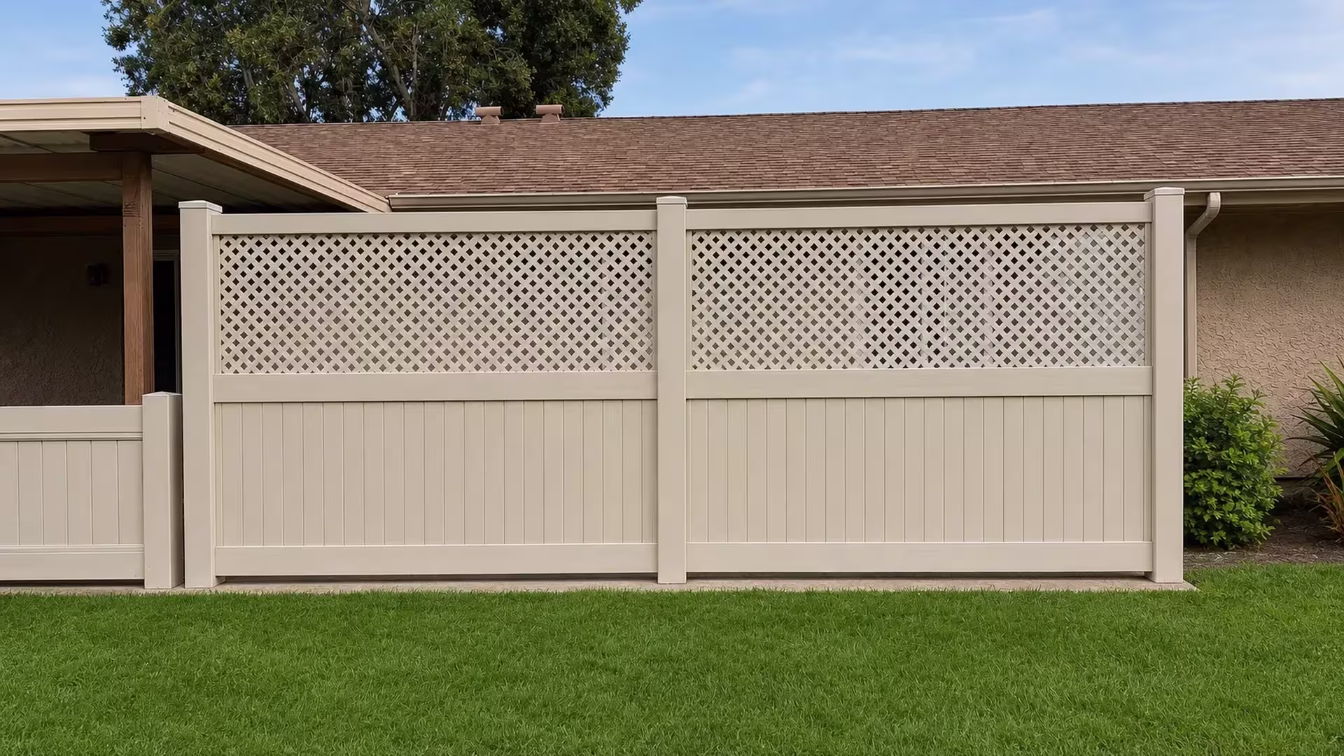 Two broad bays of Tan vinyl fence with lattice topped rails sit beside a patio cover and stucco eaves