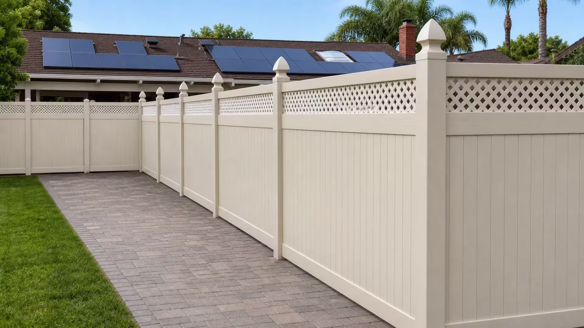 Tan vinyl privacy fence with a diamond lattice top framed by roof solar panels and a brick chimney