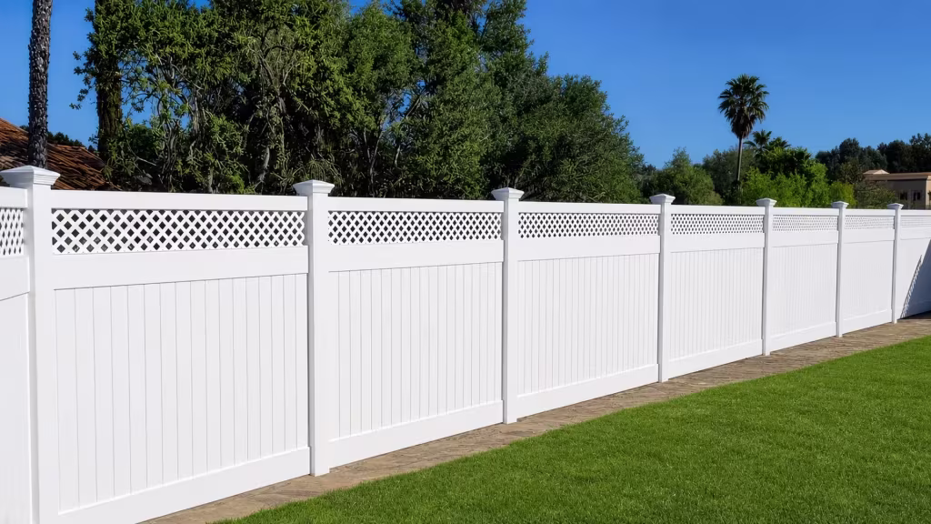 White vinyl privacy fence receding across a lawn past a stone paver strip and distant palms