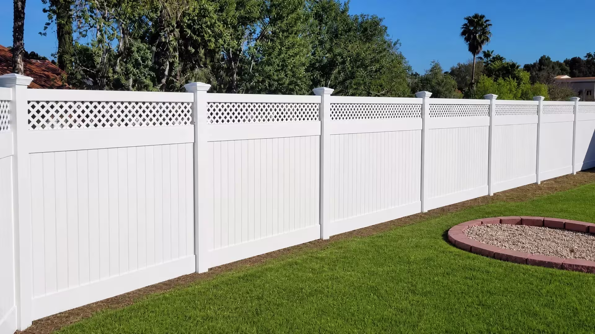 A curved gravel planting bed borders a lattice crowned White vinyl privacy fence near seven capped posts