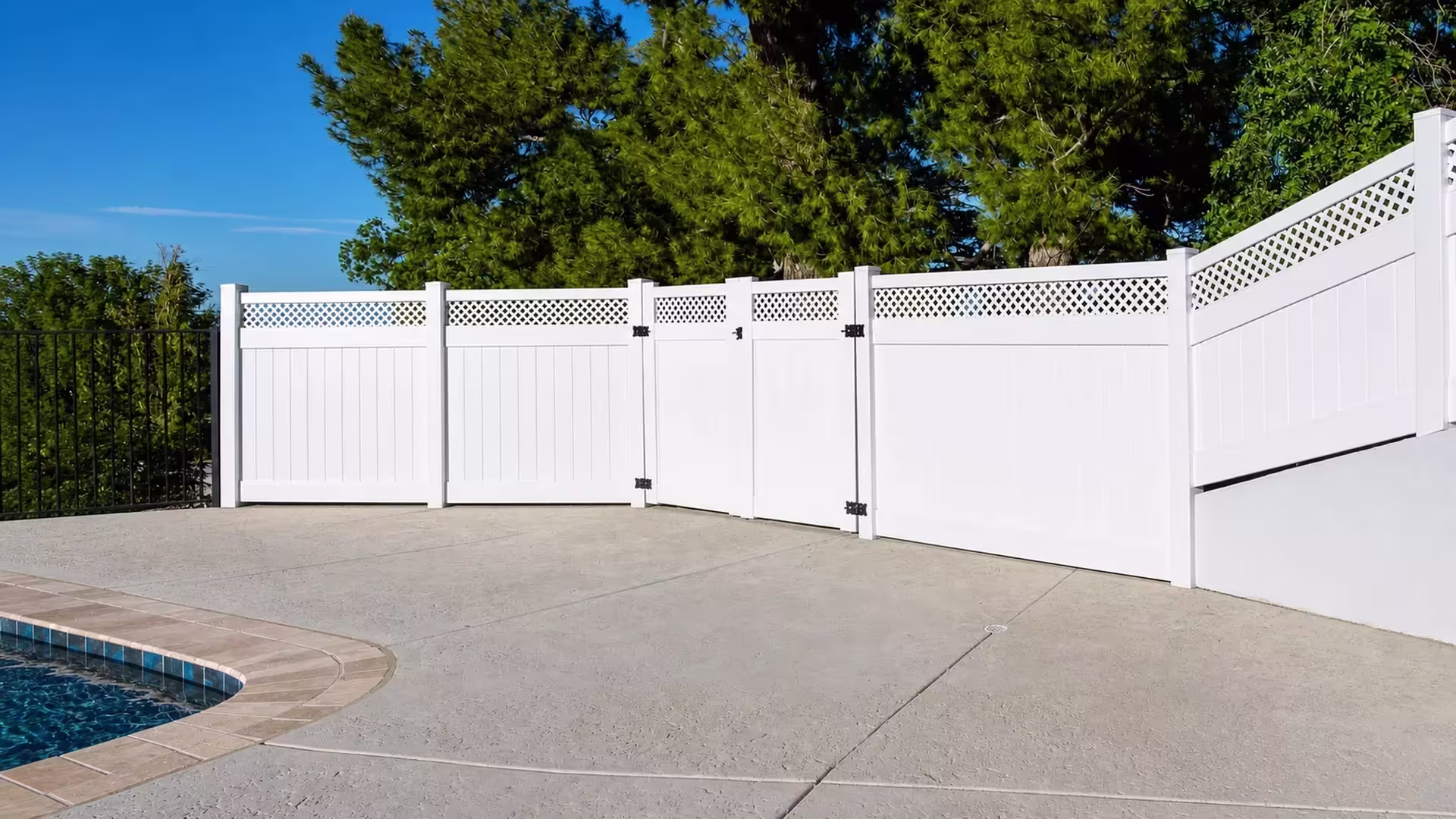 Two gate leaves meet at the center of a lattice banded White vinyl privacy fence enclosing a pool area