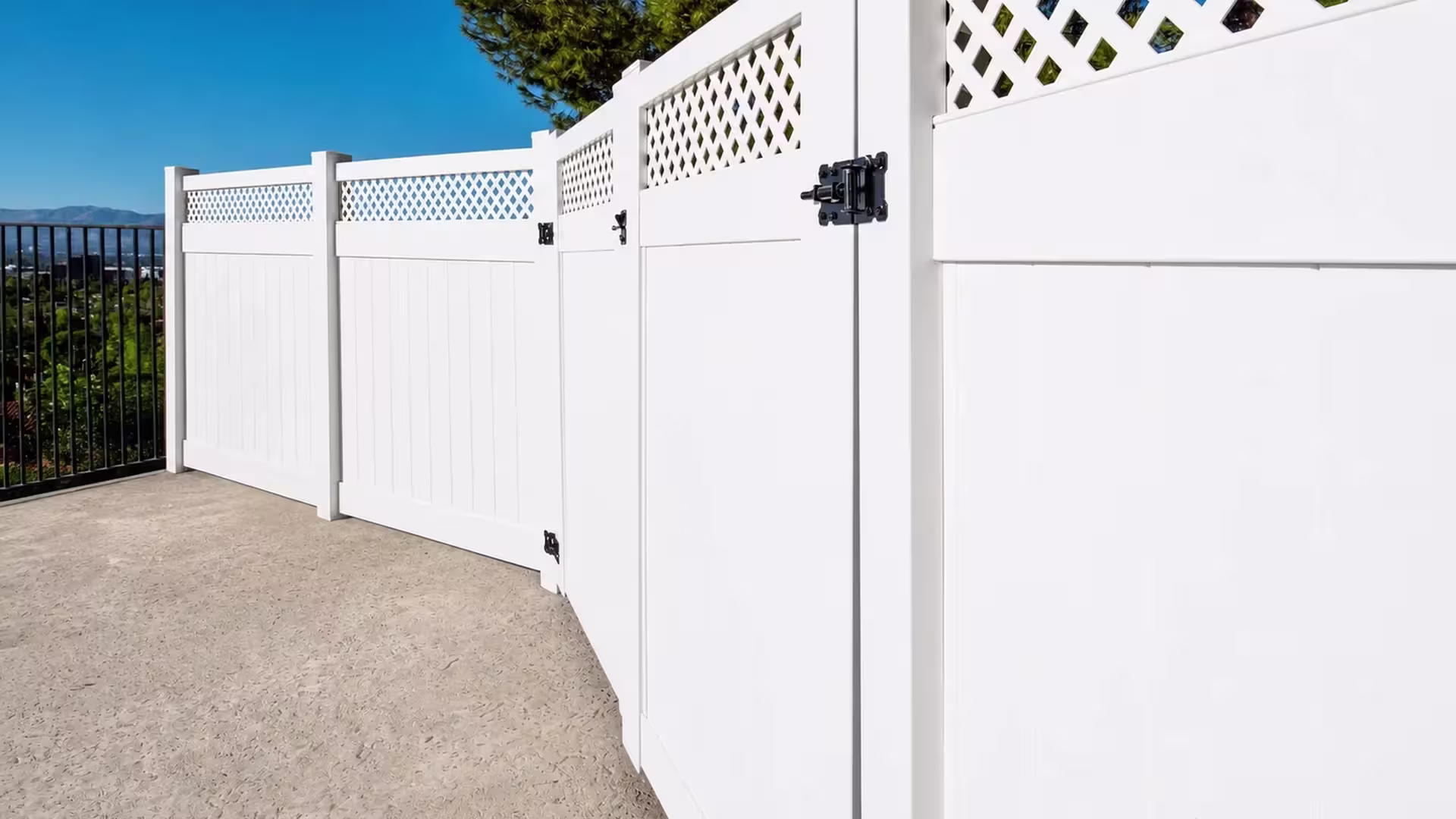 A distant city skyline and mountain ridge rise past a lattice topped White vinyl fence on an elevated patio