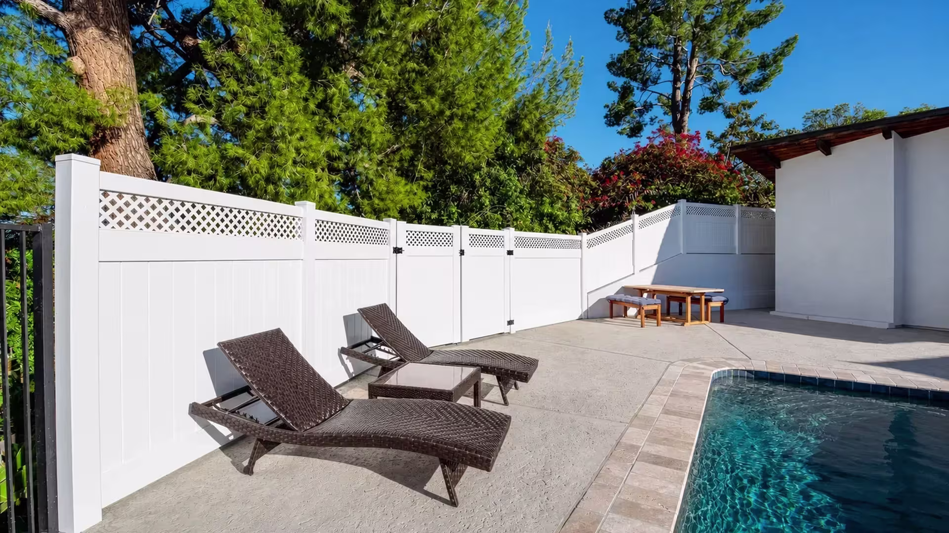 Outdoor furniture sits inside a White vinyl fence and pool deck enclosure near a black metal railing