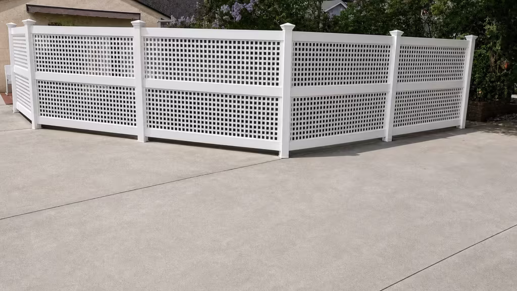 Dense square lattice fills upper and lower bays of a White vinyl privacy fence near concrete paving