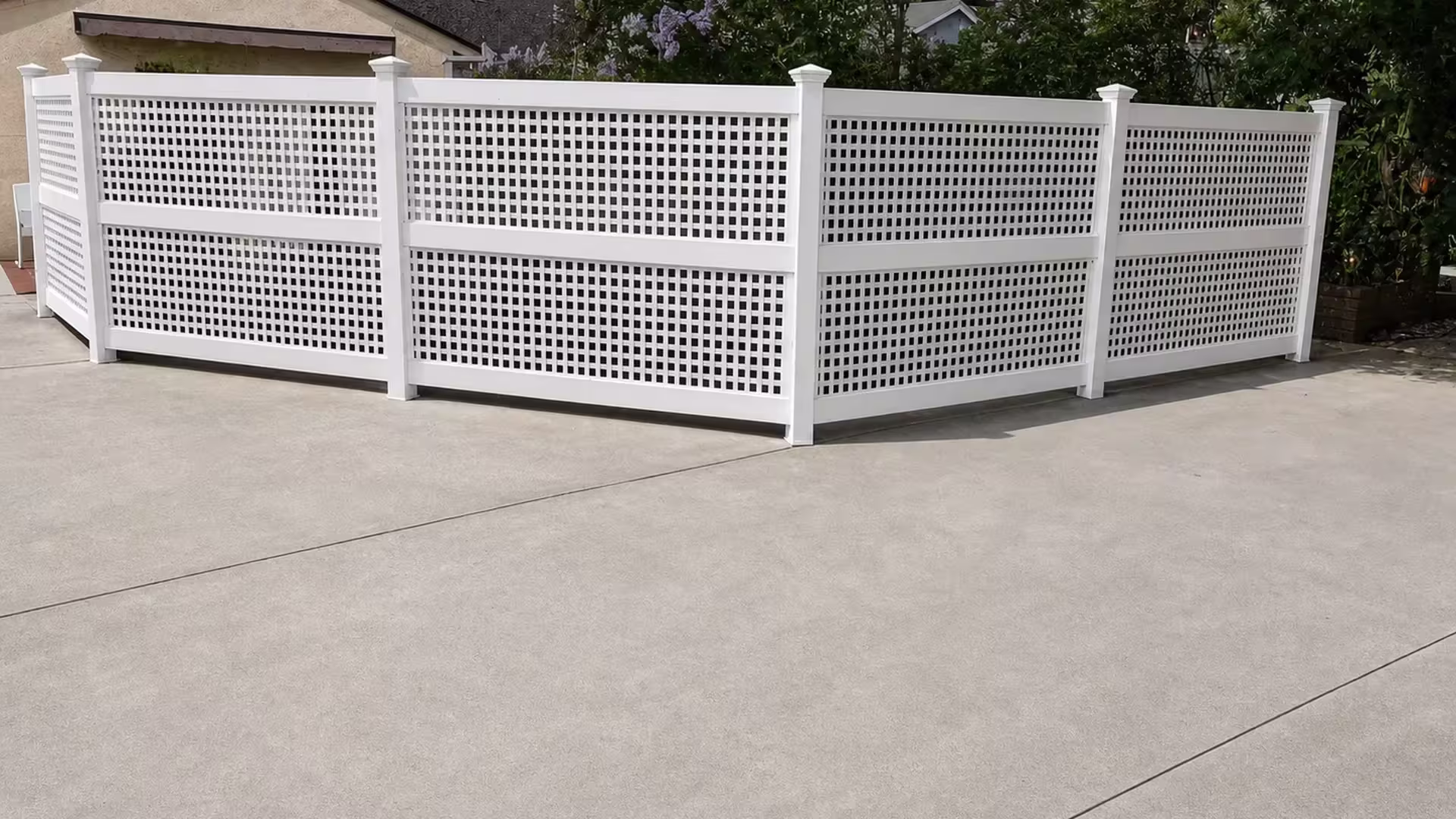 Dense square lattice fills upper and lower bays of a White vinyl privacy fence near concrete paving
