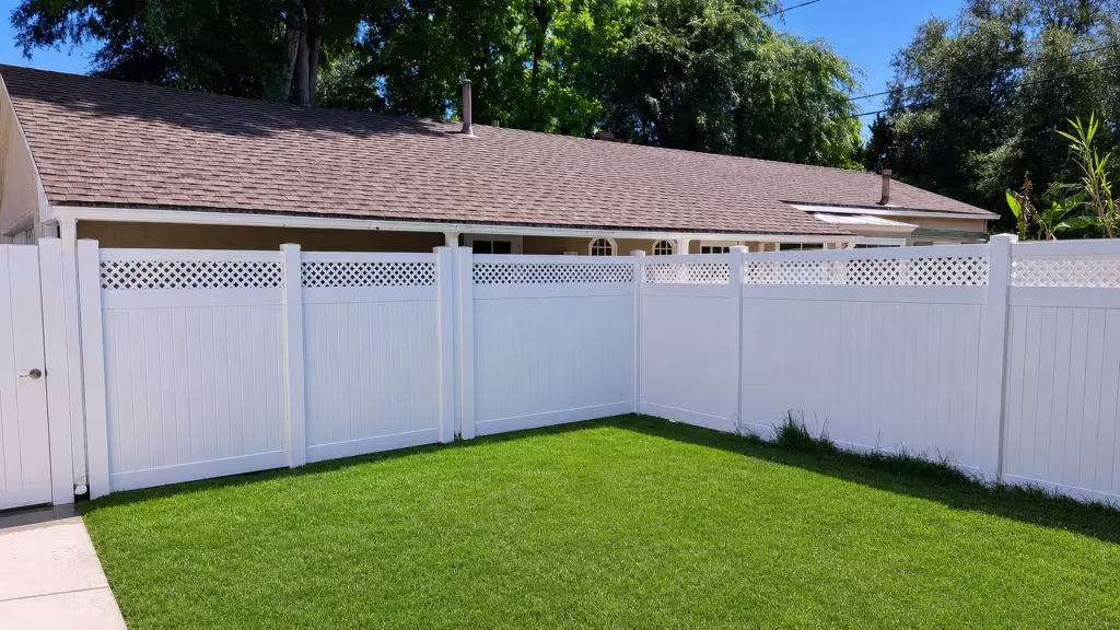 An L shaped corner turn carries a lattice topped White vinyl privacy fence past a concrete walkway
