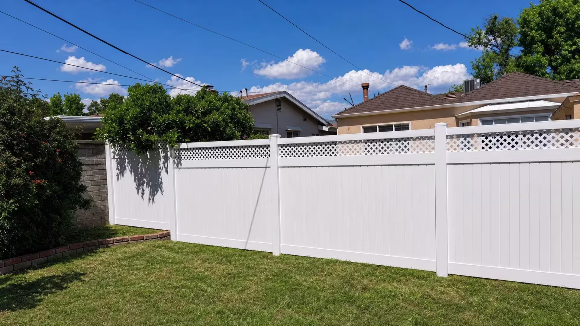 Overhead utility lines cross above four spanning panels of White vinyl fence finished with a lattice top