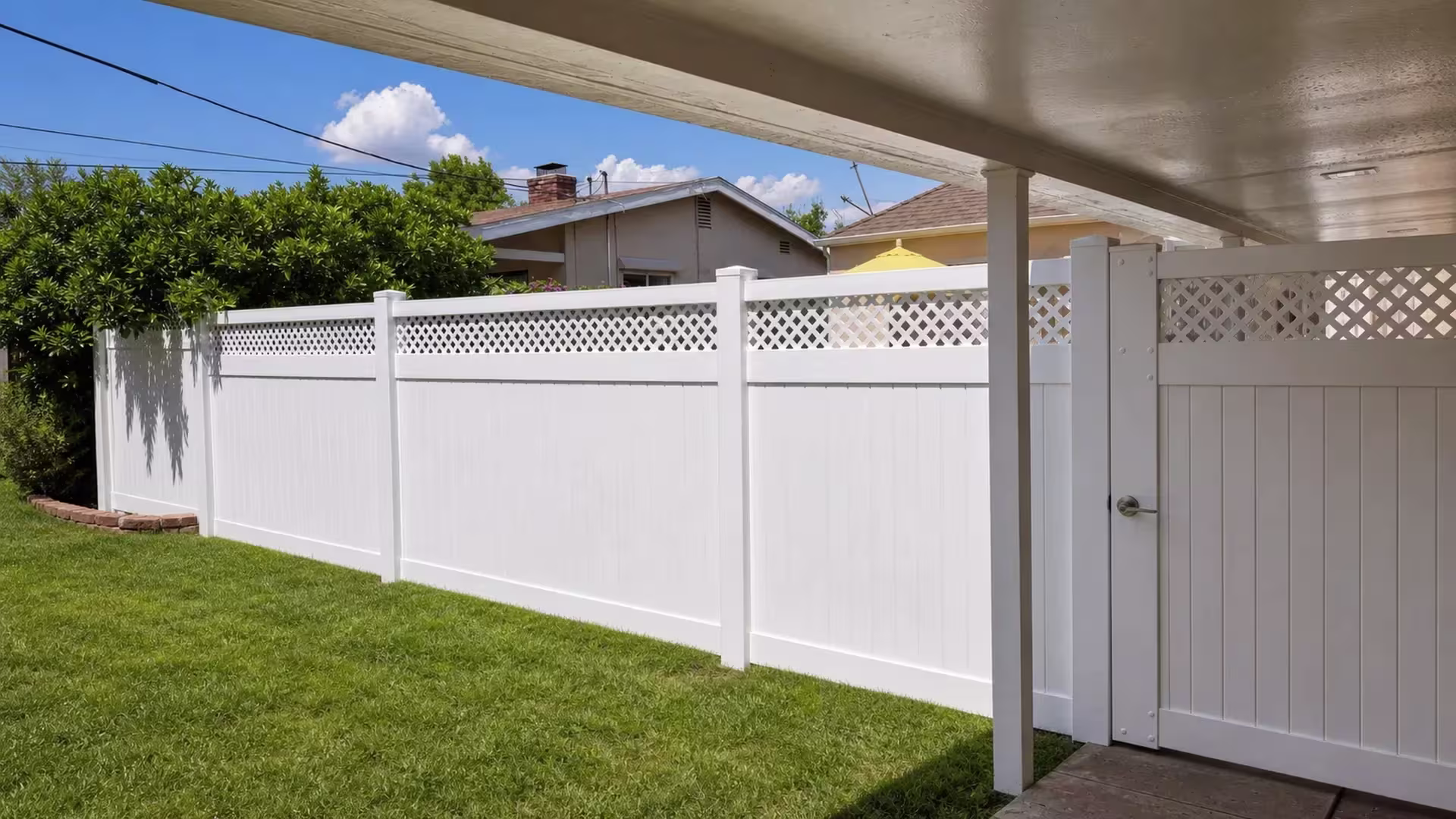 A covered patio shelters a run of White vinyl privacy fence with a lattice top leading to a pedestrian gate