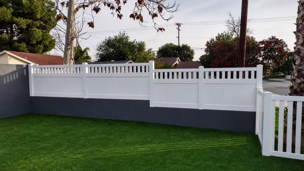 Mounted on a charcoal gray masonry wall, this White vinyl fence carries an open picket top along the street