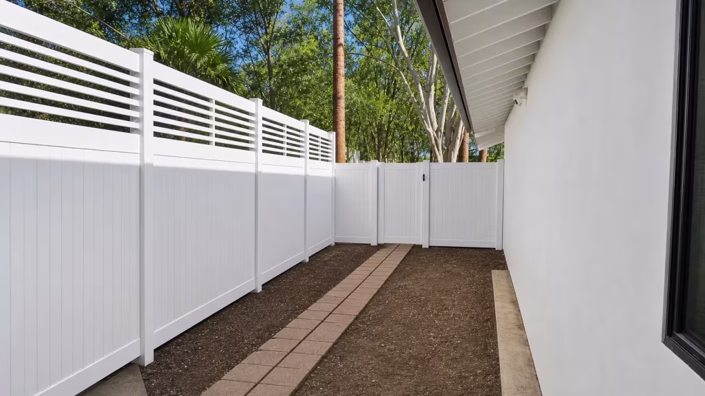 A rear gate and a stucco house paver path flank this White vinyl fence with a picket top