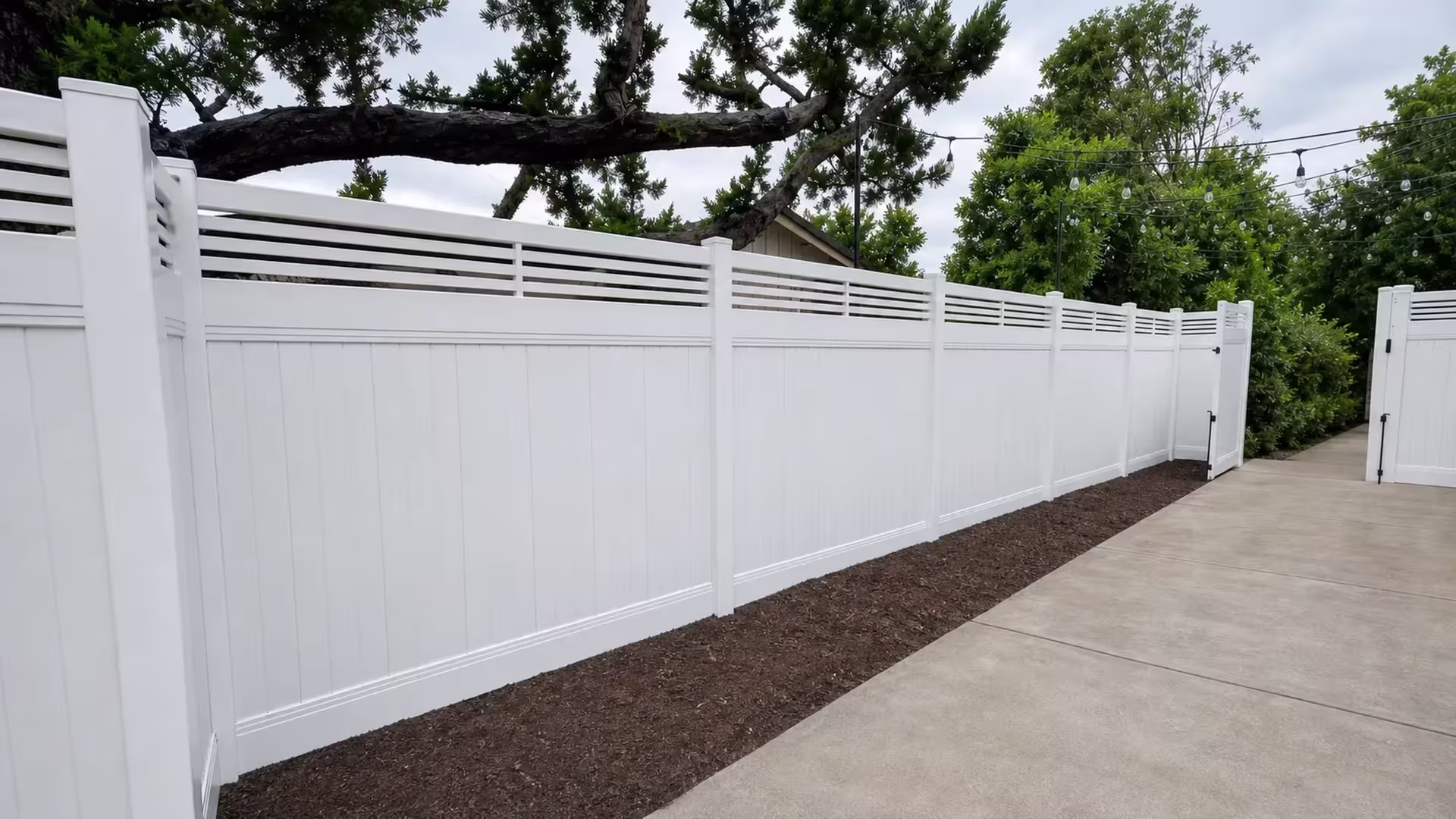 A large foreground corner post anchors this newly installed White vinyl fence with a picket top