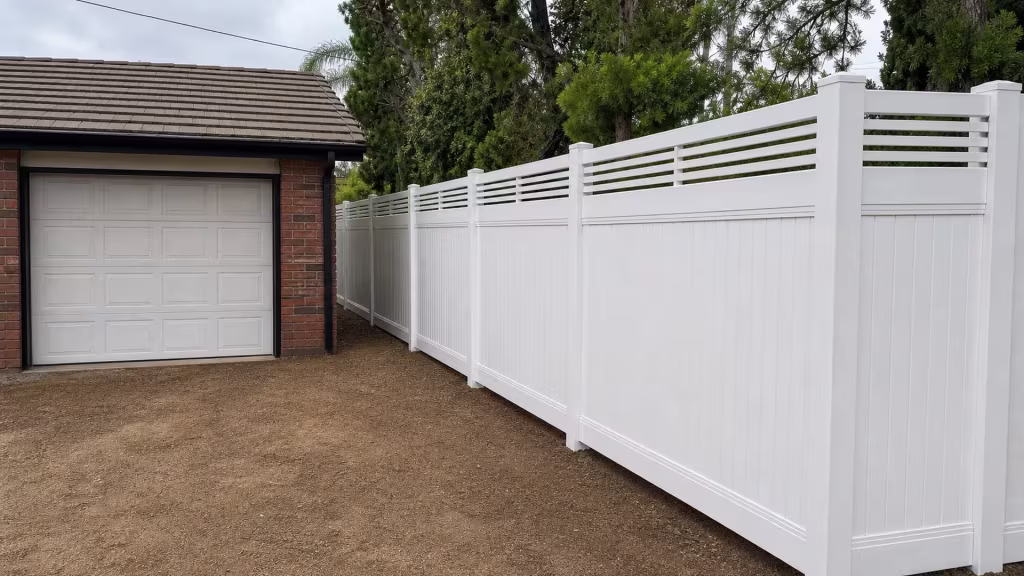 This White vinyl fence with a picket top stretches the length of a garage under overhead utility lines