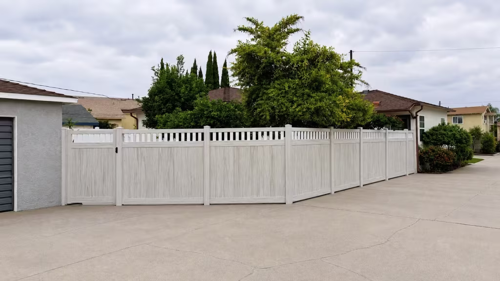 A black latch marks the stucco garage side of this White vinyl fence topped with an open picket band above the driveway