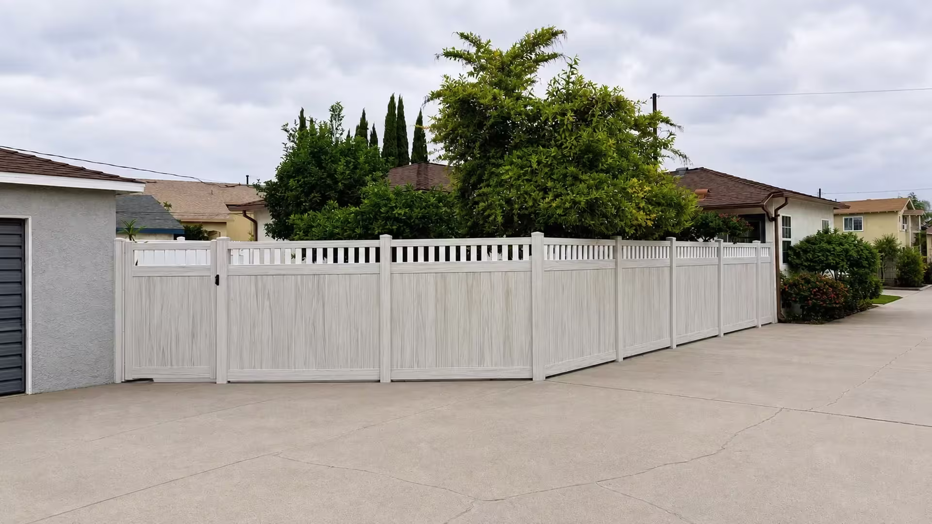 A black latch marks the stucco garage side of this White vinyl fence topped with an open picket band above the driveway