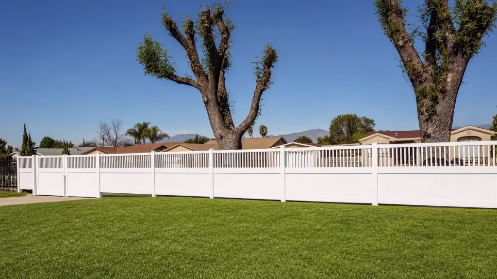 Distant mountains rise behind a long White vinyl fence with an open picket top crossing the level lawn