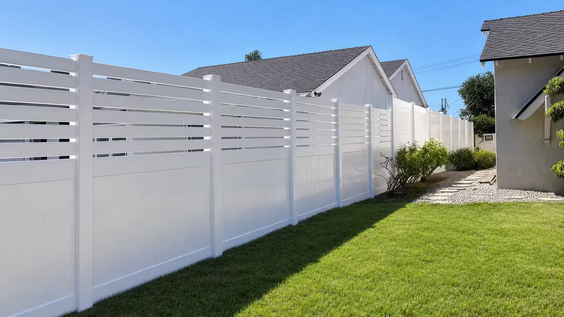 Newly installed White vinyl fence runs diagonally past a gravel and stepping-stone strip toward the rear yard