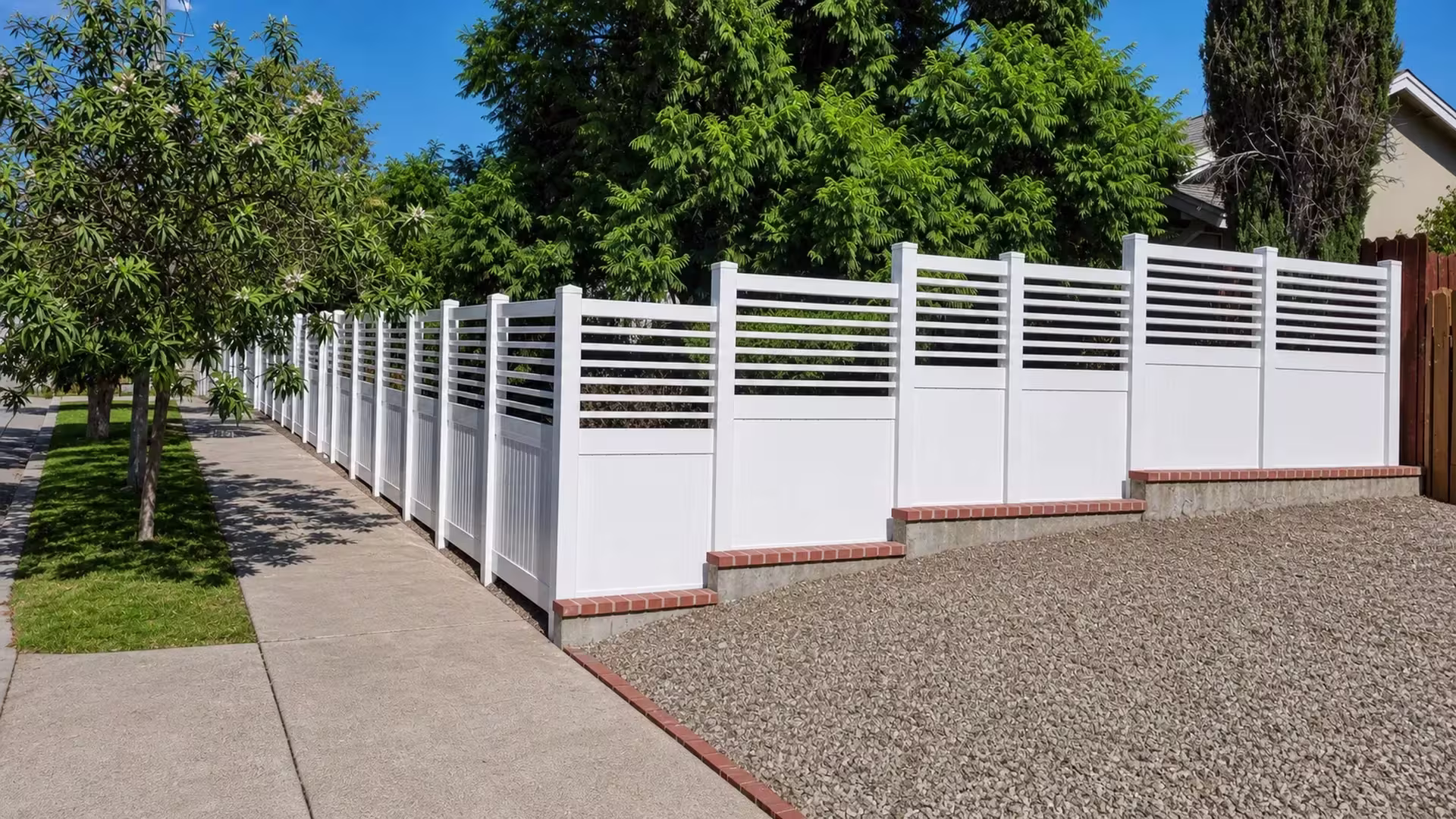 Brick-capped footings step this White vinyl fence with a picket top past a brown wood boundary fence