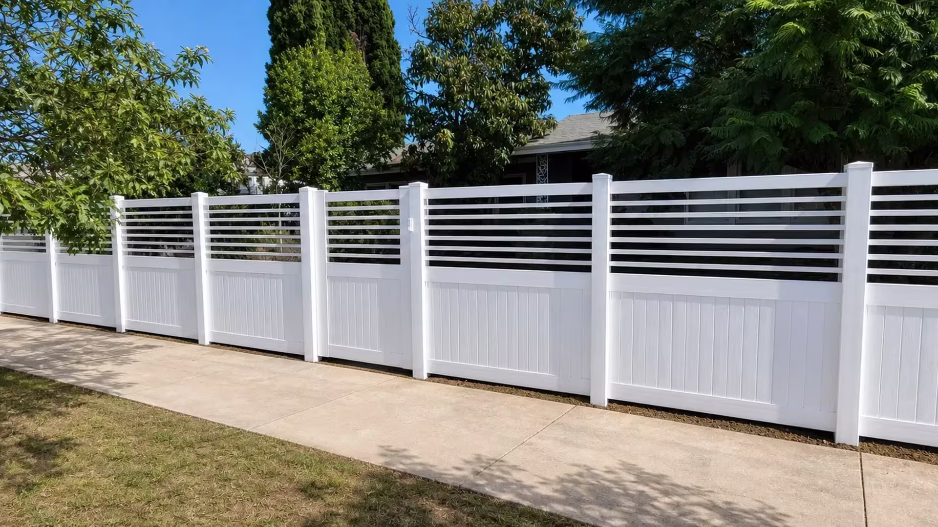 Seven square posts space out this White vinyl fence with a picket top toward a concrete path and the roofline