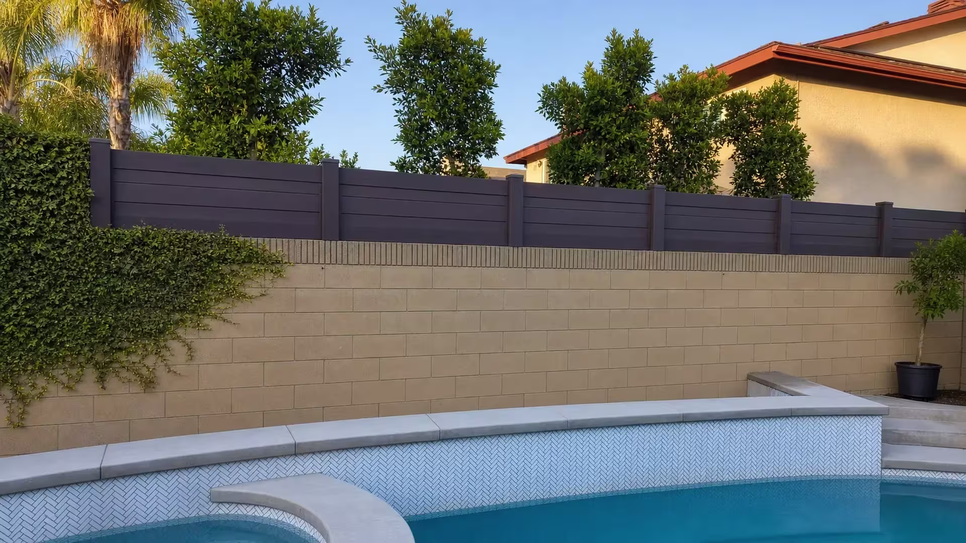 Dark Walnut vinyl privacy topper mounted along a tan retaining wall beside a swimming pool and spa
