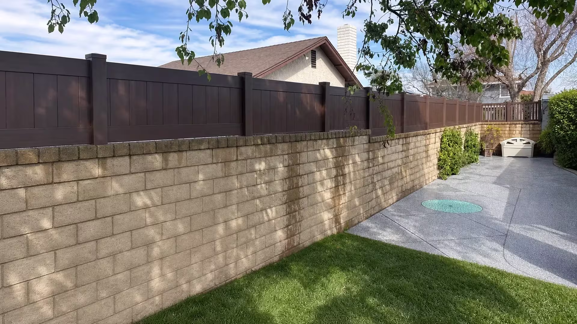Dark Walnut vinyl wall topper receding across a tan masonry wall past the house patio and chimney