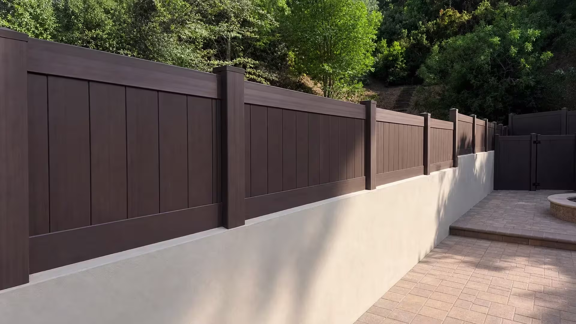 Stepped Dark Walnut vinyl wall topper follows the sloped grade of a cream stucco wall toward a matching gate return