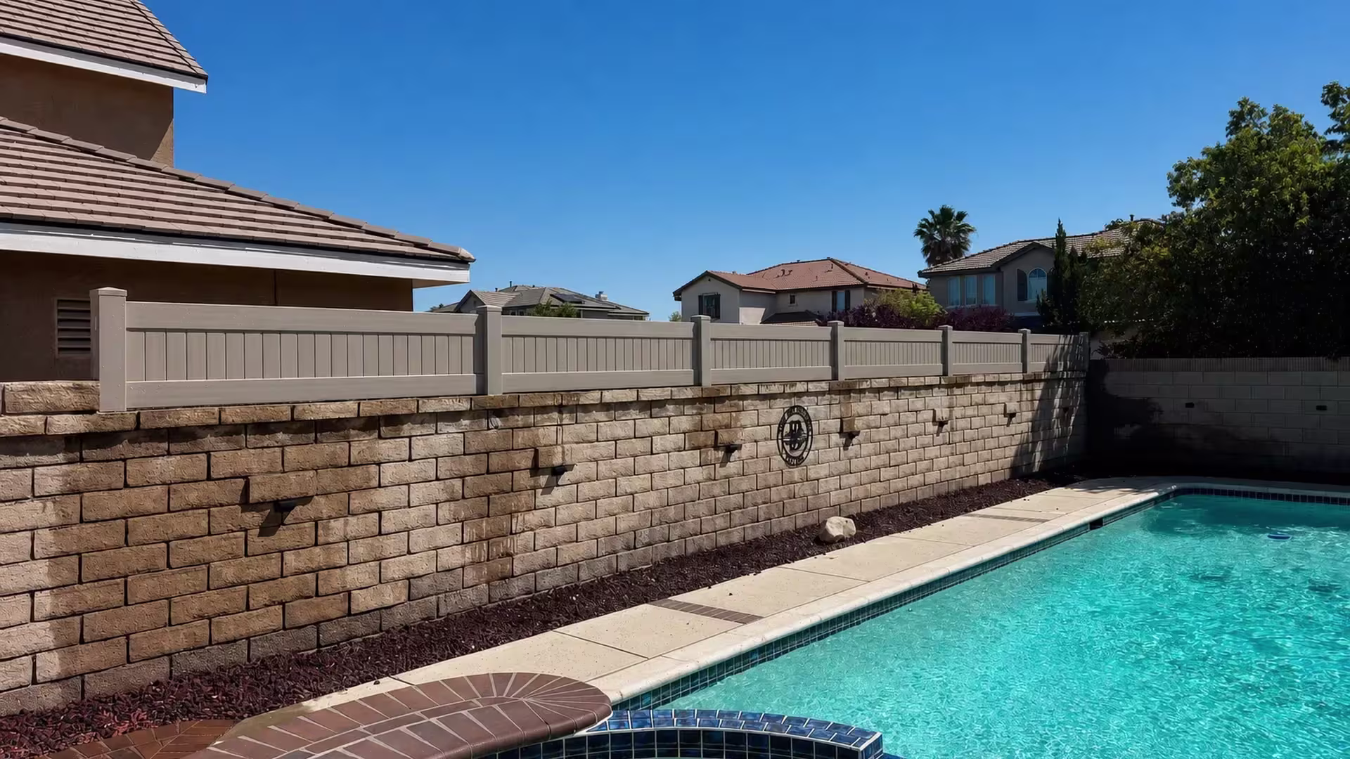 Tan vinyl vertical privacy topper tops a block pool wall fitted with a decorative wall medallion and lights
