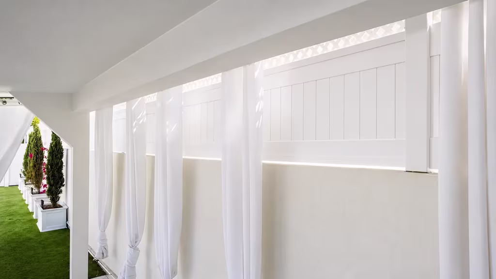 White vinyl wall topper adds a lattice band above solid boards beneath a covered patio hung with drapery