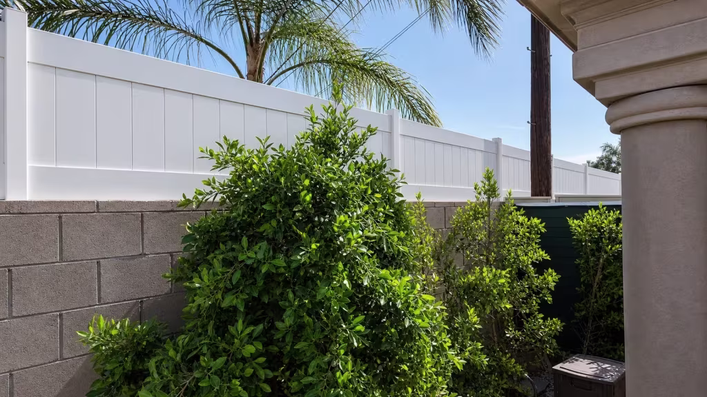 Palm fronds arch over a White vinyl wall topper set beside a stucco house column on the block wall
