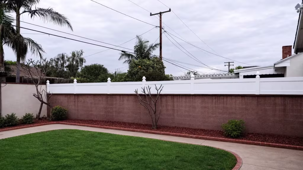 White vinyl wall topper with pointed post caps borders a curved backyard lawn near a pergola
