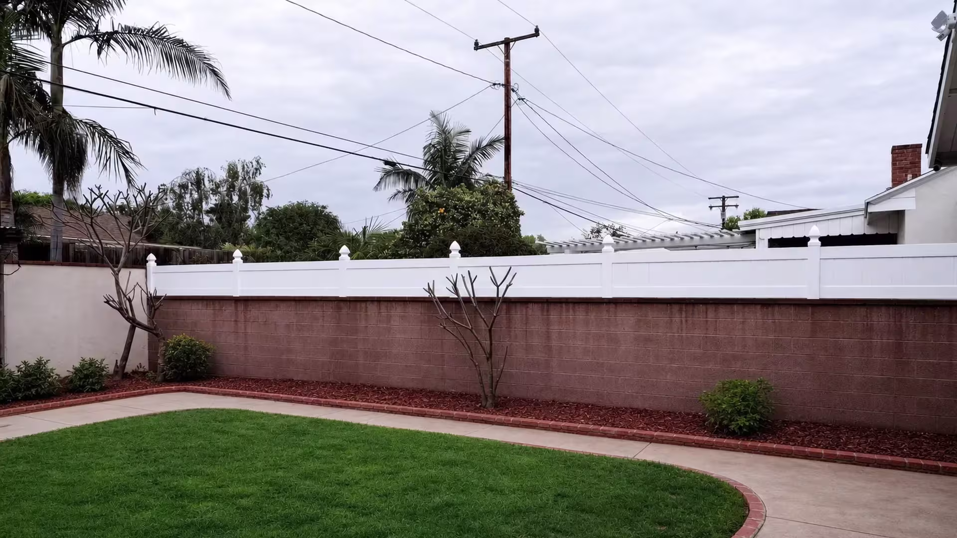 White vinyl wall topper with pointed post caps borders a curved backyard lawn near a pergola