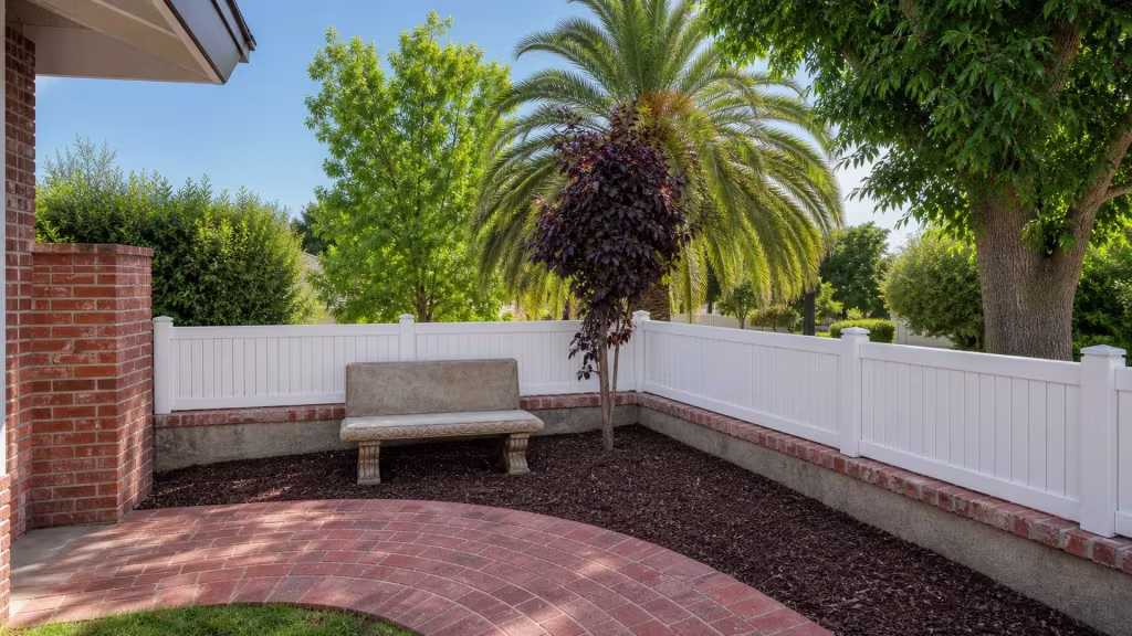 Front yard corner holds a low White vinyl privacy picket wall topper beside a brick column and stone bench