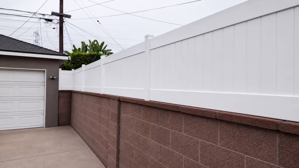Reddish-brown block wall wears a continuous White vinyl privacy wall topper beside an attached garage structure