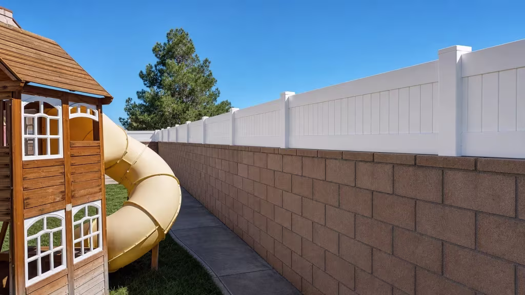 Children's playhouse and tube slide sit beside a White vinyl privacy wall topper on the brown block wall