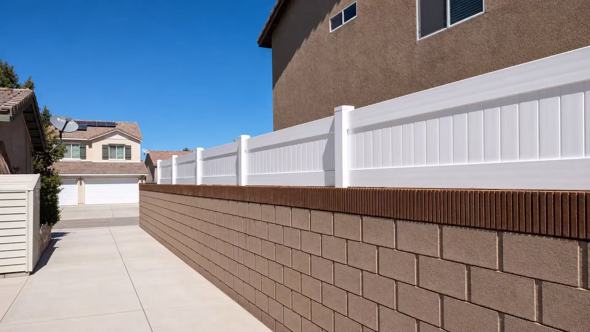 White vinyl privacy wall topper follows a brown block wall past a narrow side yard beneath rooftop solar panels
