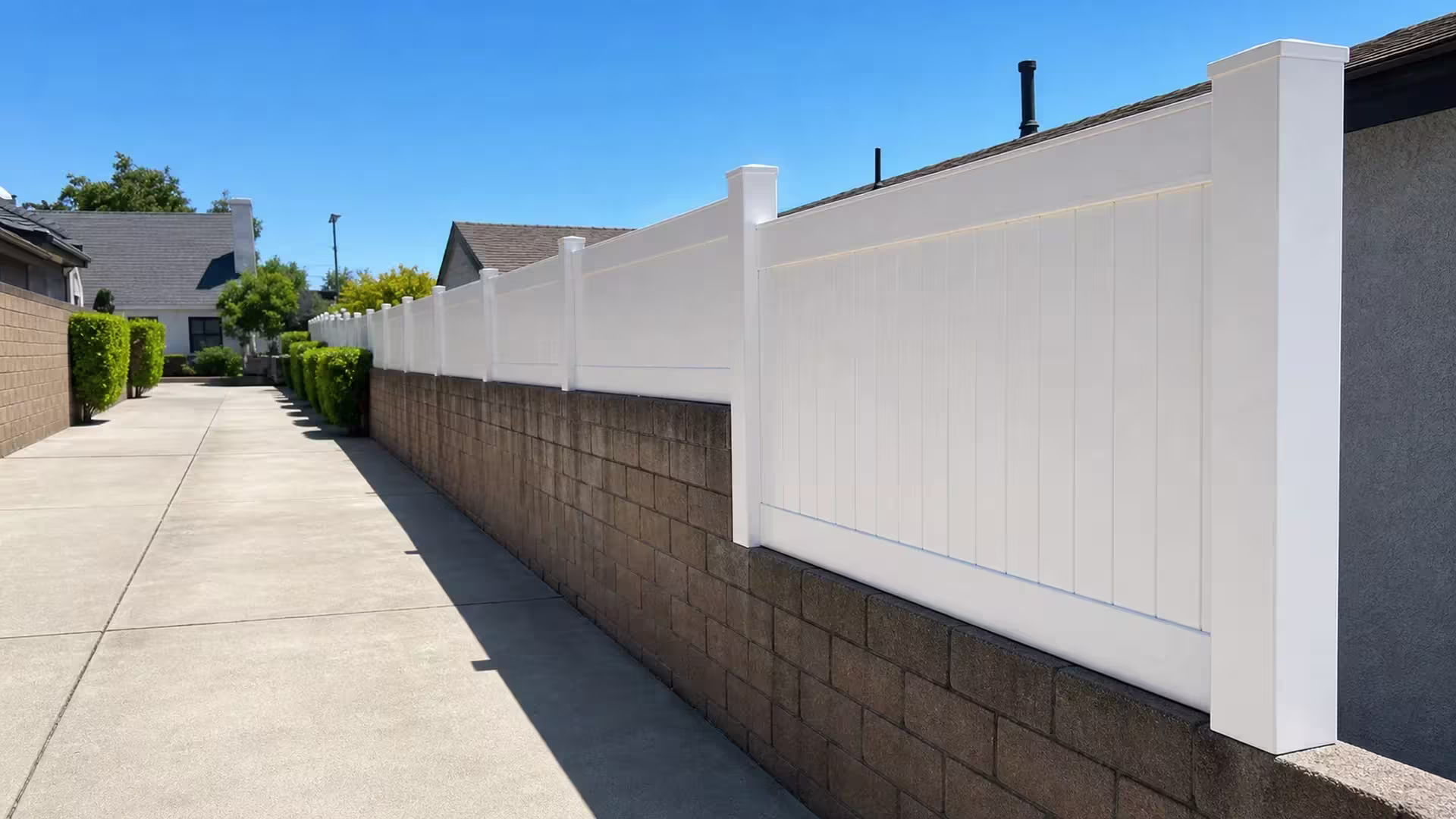 Narrow concrete alley is bordered by a White vinyl privacy wall topper on a long brown block wall