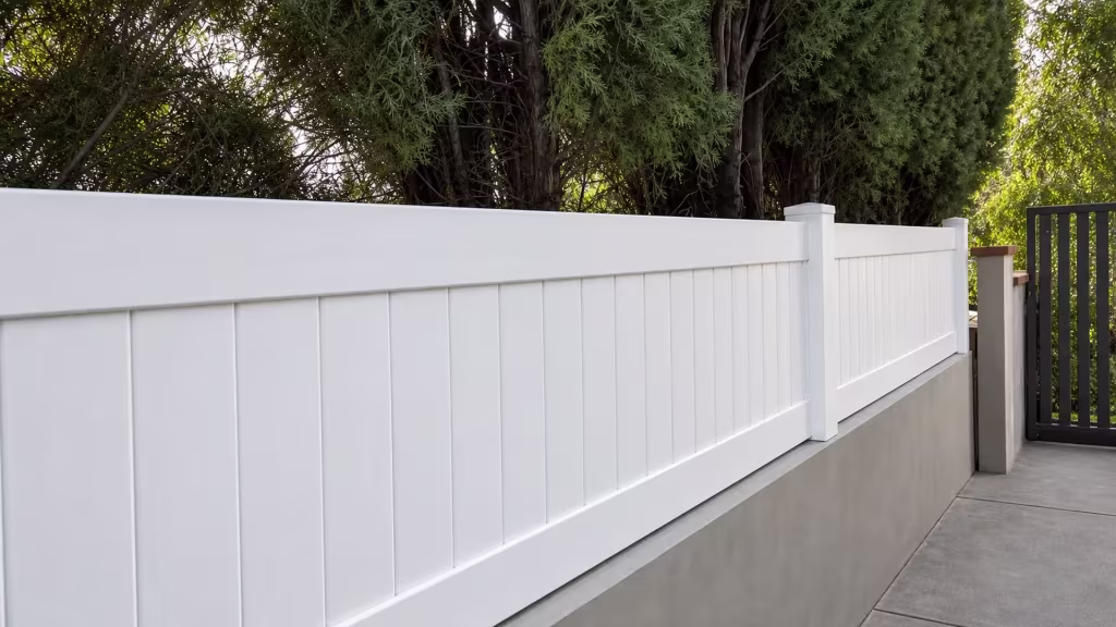 Dark metal gate and masonry posts mark the end of a White vinyl privacy wall topper run