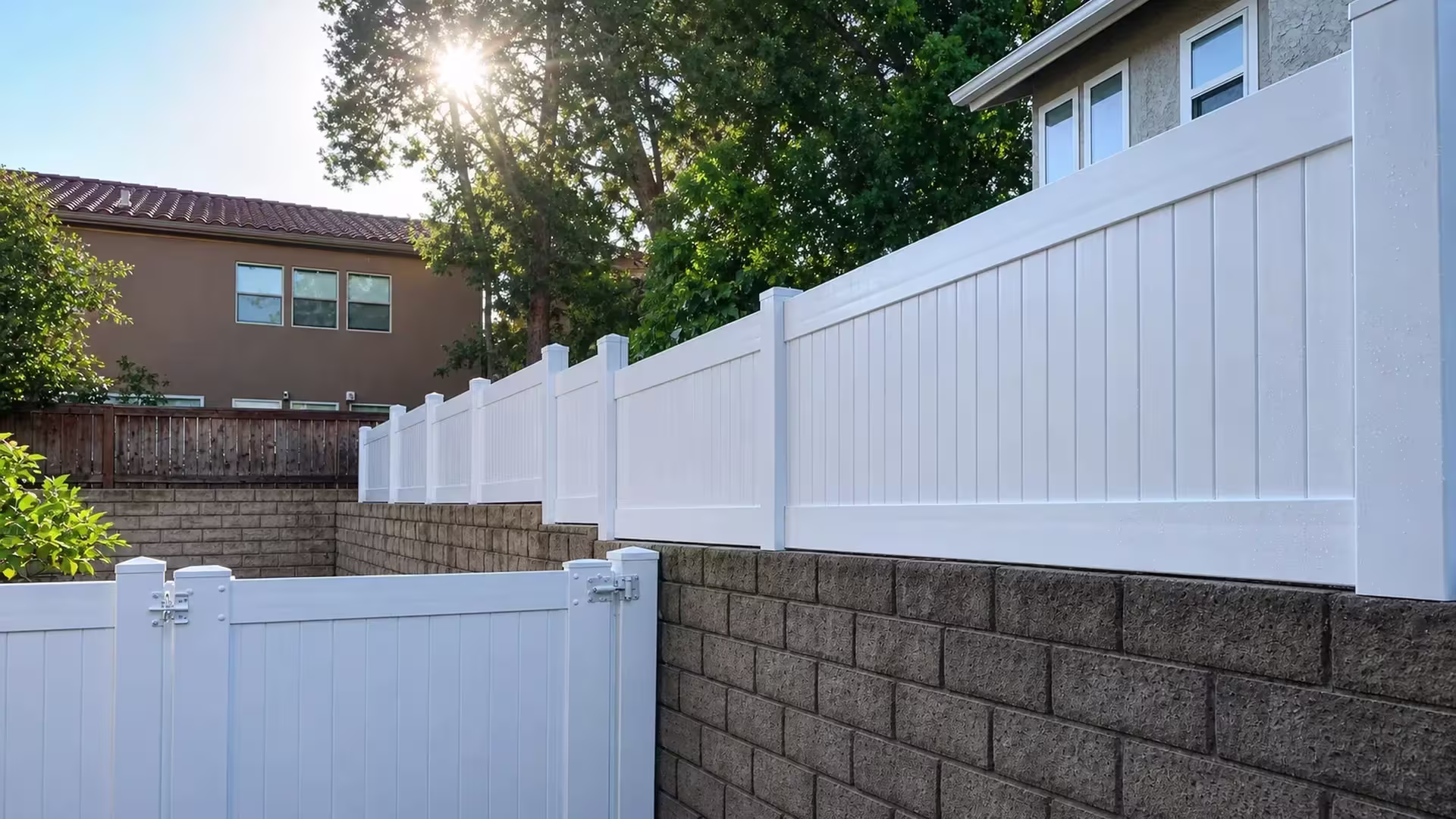 Neighboring wood fence line meets a White vinyl privacy wall topper stepping down the masonry wall