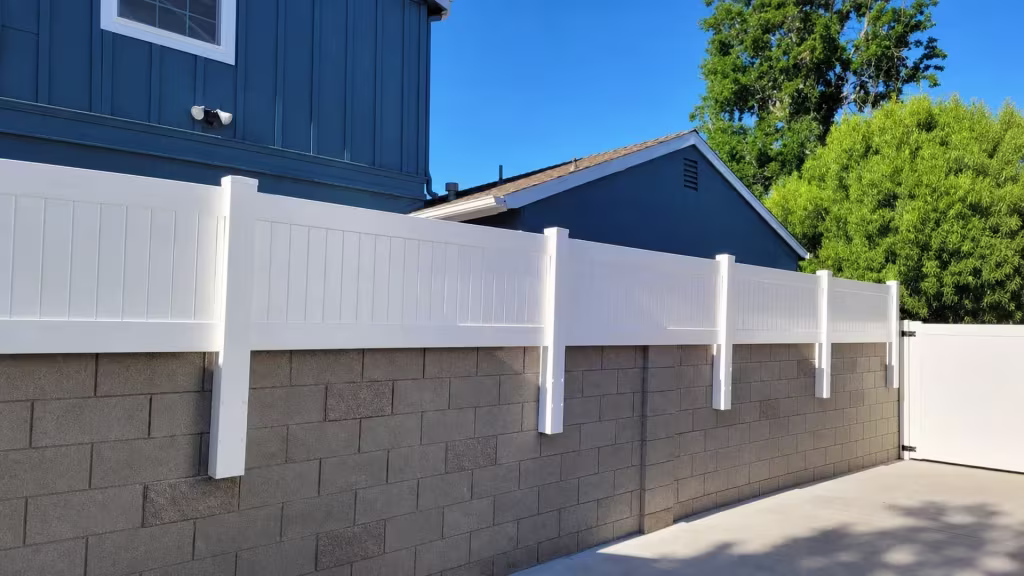 Two blue buildings flank a White vinyl privacy wall topper along the shared gray block wall