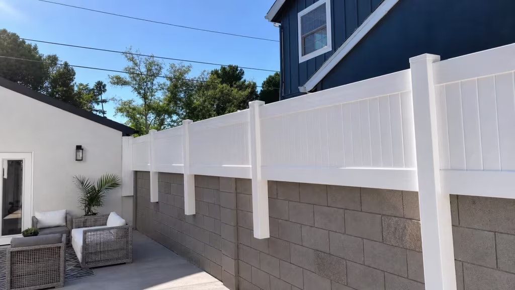 Dark blue house and outdoor furniture stand next to a White vinyl privacy wall topper on the gray block wall