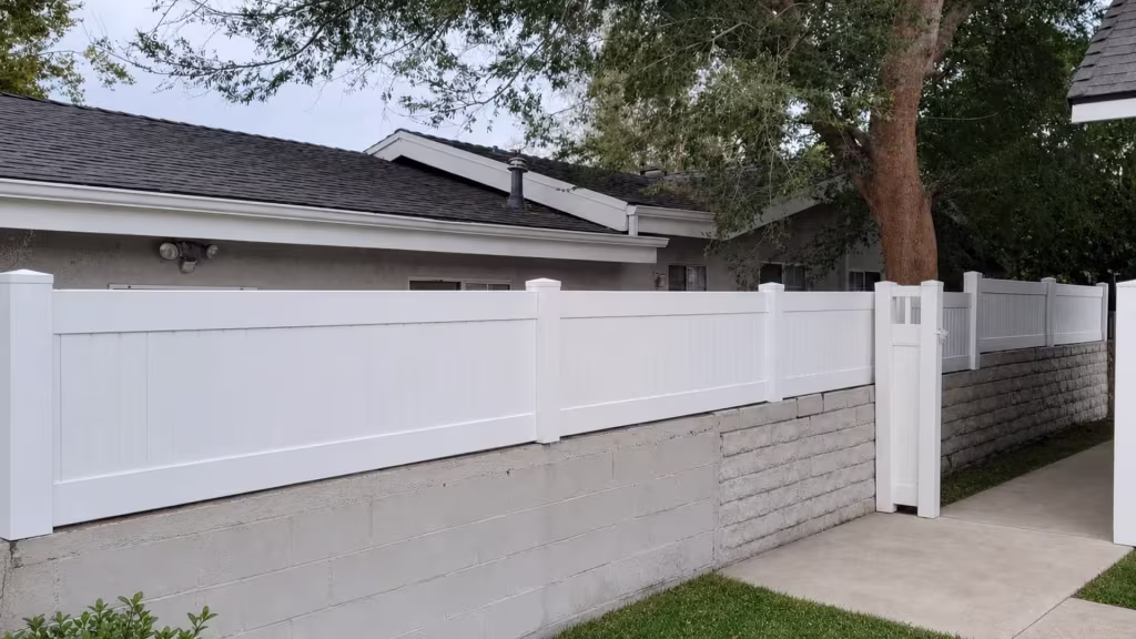 Mature tree canopy spreads over a White vinyl privacy wall topper along the textured masonry wall